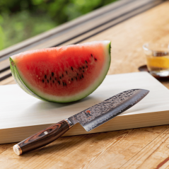 Miyabi 6000 MCT - Couteau Santoku Japonais Lame 18 cm - Le couteau disposé sur une planche à découper à côté d'un melon tranché.