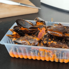 Barquette frite plastique remplie de moules en sauce.