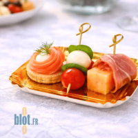 Présentation cocktail salée sur mini assiette carrée or avec saumon, fromage et brochettes apéritives.