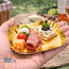 Assiette carrée or tenue en main avec assortiment apéritif salé en situation extérieure.